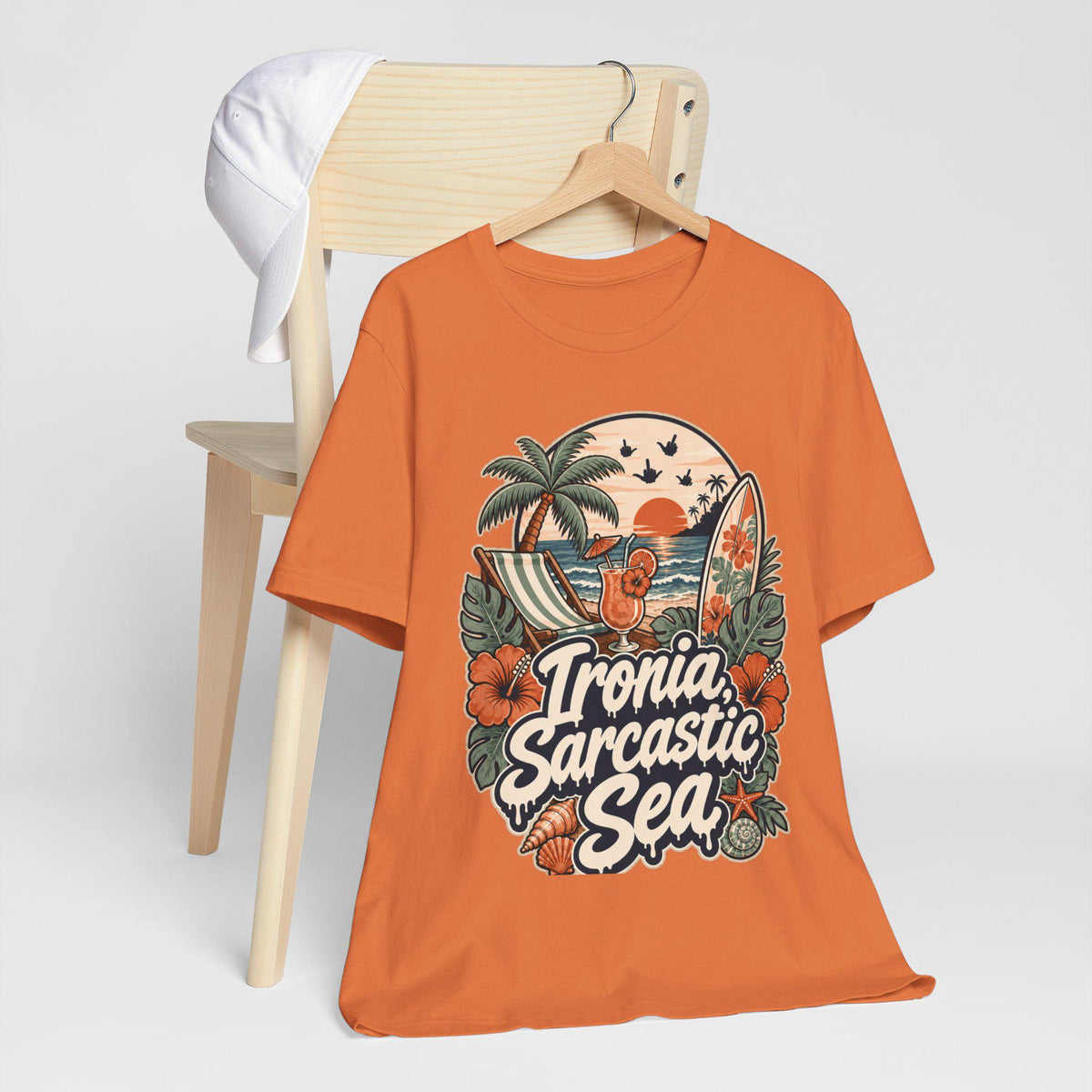 The "Ironia, Sarcastic Sea" retro beach T-shirt by SarcasmArt in burnt orange hanging on a wooden chair.