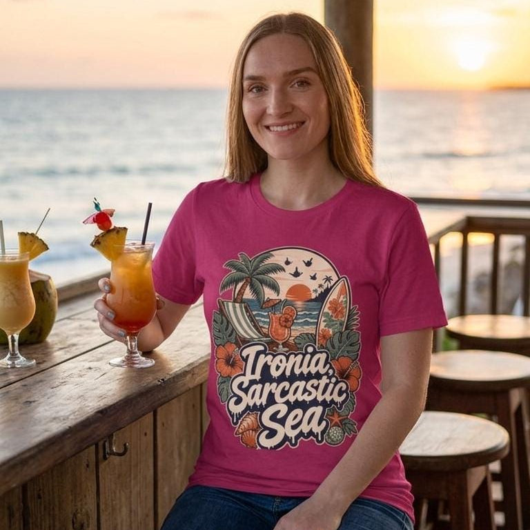 Smiling woman at a beach bar at sunset wearing the "Ironia, Sarcastic Sea" retro beach T-shirt by SarcasmArt in raspberry pink – an anti-social vacation tee with a vintage tropical beach scene with palm tree, deck chair, cocktail, surfboard, sunset, hibiscus flowers and shells around the script Ironia, Sarcastic Sea.