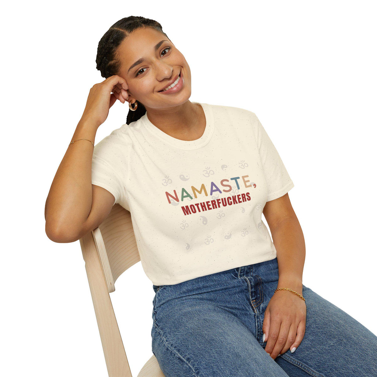 Smiling woman sitting on a chair wearing the "Namaste, Motherfuckers" funny yoga T-shirt by SarcasmArt in Natural.
