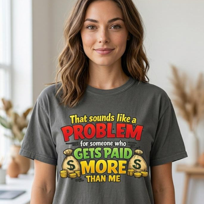 Woman wearing the "That Sounds Like a Problem for Someone Who Gets Paid More Than Me" sarcastic coworker T-shirt by SarcasmArt in Pepper (washed charcoal) – a Comfort Colors 1717 unisex tee with bold red, yellow and green retro lettering reading That sounds like a PROBLEM for someone who GETS PAID MORE THAN ME with gold coins.