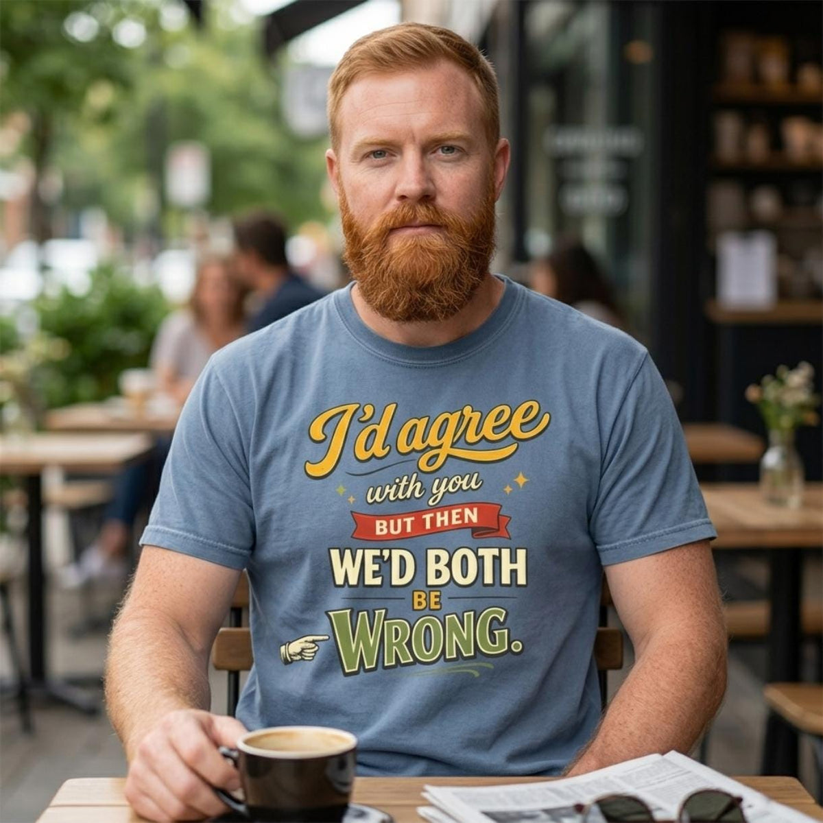 Bearded man with a coffee at a café table wearing the "I'd Agree With You But Then We'd Both Be Wrong" sarcastic quote T-shirt by SarcasmArt in Blue Jean – a Comfort Colors 1717 unisex tee with vintage script and block lettering reading I'd agree with you but then WE'D BOTH BE WRONG in gold, red, cream and olive.