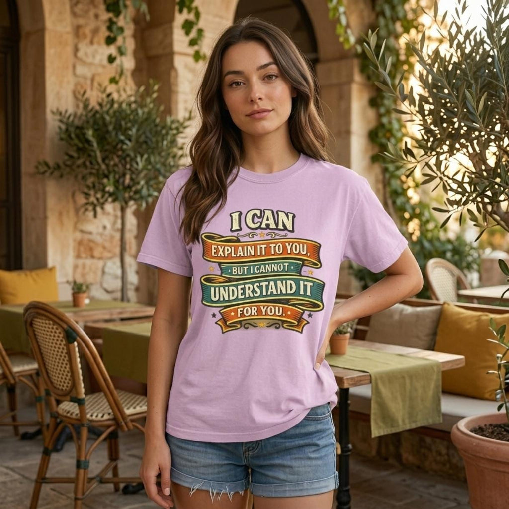 Woman in a sunny café courtyard wearing the "I Can Explain It to You, But I Can't Understand It for You" sarcastic teacher T-shirt by SarcasmArt in Orchid (soft pink) – a Comfort Colors 1717 unisex tee with vintage ribbon banners reading I CAN EXPLAIN IT TO YOU BUT I CAN'T UNDERSTAND IT FOR YOU in orange, green and cream.