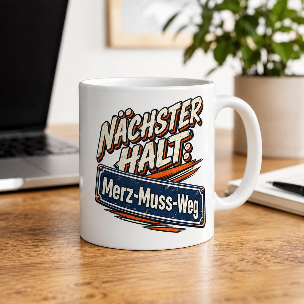 "Nächster Halt: Merz-Muss-Weg" German political satire coffee mug by SarcasmArt: white 11 oz ceramic mug with retro comic lettering NÄCHSTER HALT: above a blue street-sign style plate reading Merz-Muss-Weg with orange speed lines, on a wooden desk next to a laptop.
