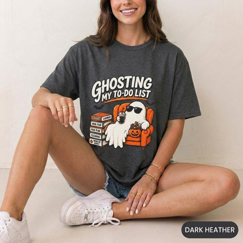 Woman sitting on the floor wearing the "Ghosting My To-Do List" retro Halloween procrastinator T-shirt by SarcasmArt in Dark Heather – a Gildan Softstyle 64000 tee.