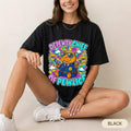 Woman sitting wearing the "Depewty Chief of Pewlice" capybara meme T-shirt by SarcasmArt in Black – a Bella+Canvas 3001 unisex tee with a capybara police officer in sunglasses and a blue uniform with a badge, surrounded by colorful comic bursts and DEPEWTY CHIEF OF PEWLICE lettering.