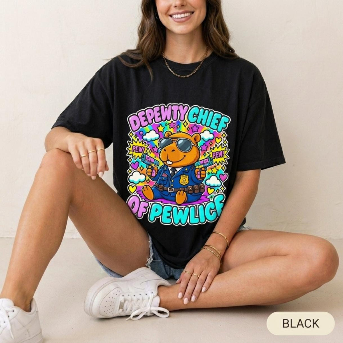 Woman sitting wearing the "Depewty Chief of Pewlice" capybara meme T-shirt by SarcasmArt in Black – a Bella+Canvas 3001 unisex tee with a capybara police officer in sunglasses and a blue uniform with a badge, surrounded by colorful comic bursts and DEPEWTY CHIEF OF PEWLICE lettering.