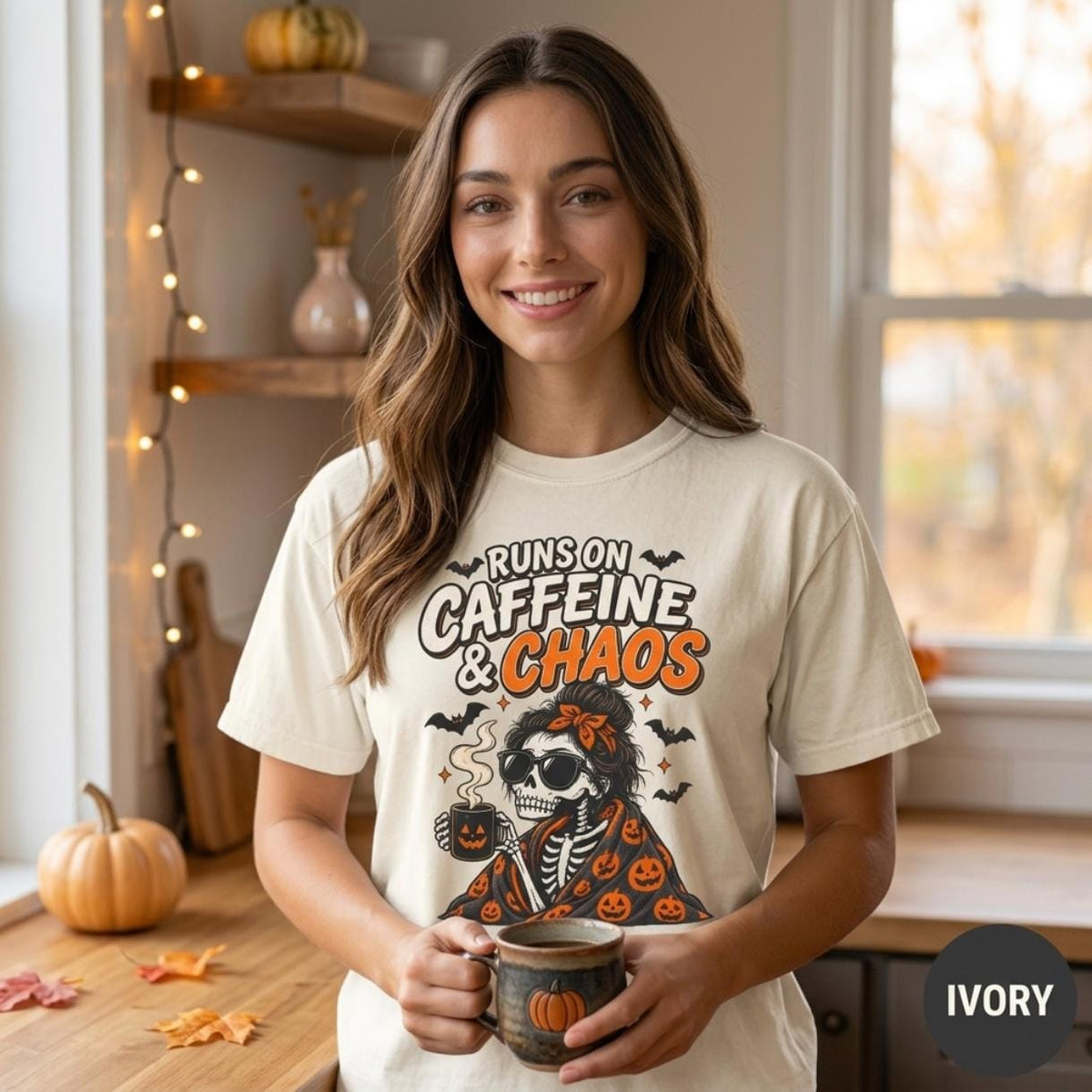 Woman holding a coffee mug in a cozy autumn home wearing the "Runs on Caffeine & Chaos" skeleton coffee Halloween T-shirt by SarcasmArt in Ivory, a funny spooky season shirt.