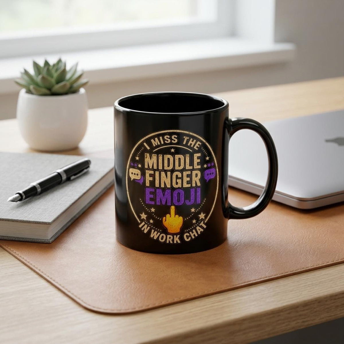 The "I Miss the Middle Finger Emoji in Work Chat" black office coffee mug by SarcasmArt on a wooden office desk next to a notebook and laptop – a sarcastic coworker gift.