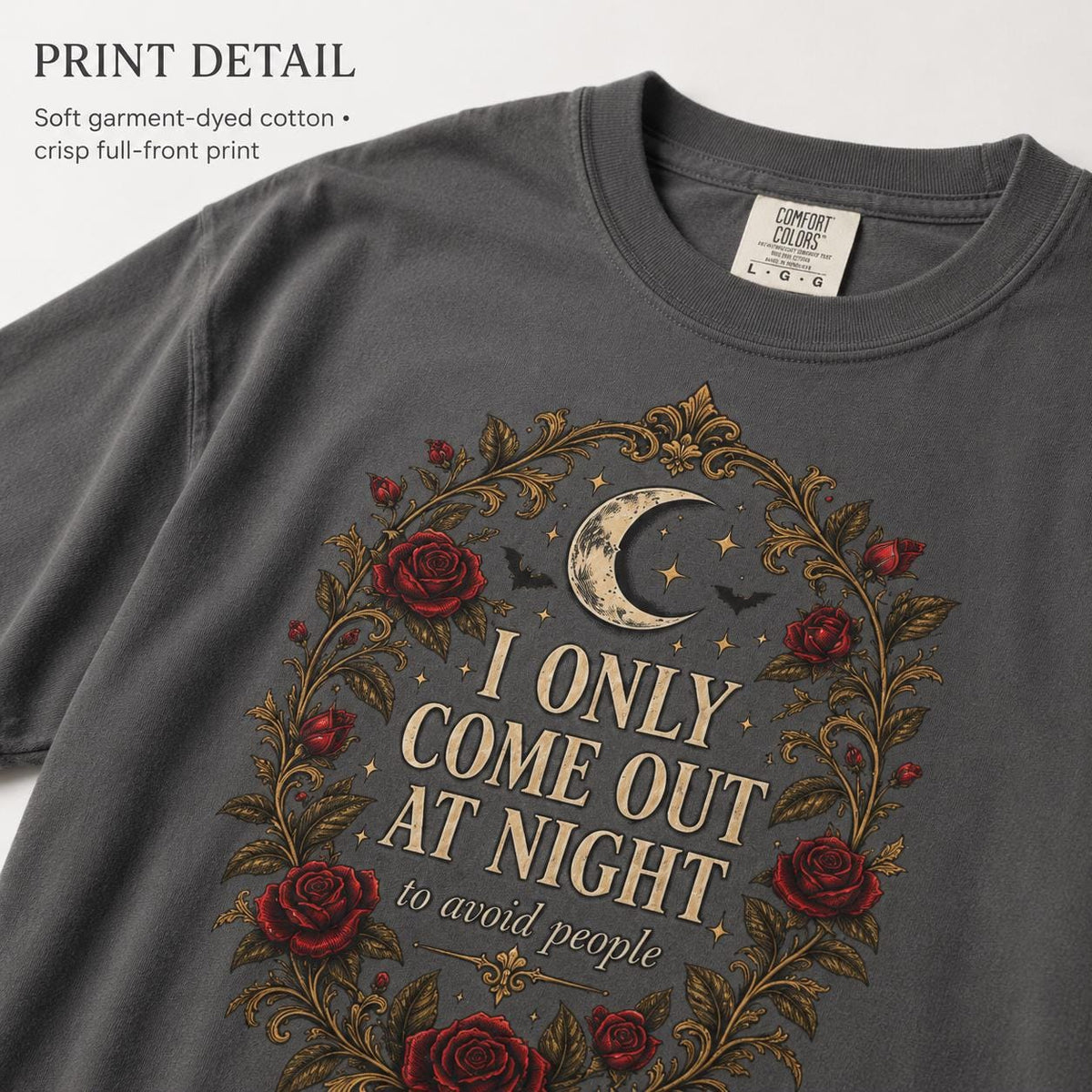 Print detail of the "I Only Come Out at Night" romantic gothic vampire T-shirt by SarcasmArt on Pepper (washed charcoal): a crescent moon, bats and dark red Victorian roses in a gold filigree frame around the words I ONLY COME OUT AT NIGHT, on soft garment-dyed Comfort Colors 1717 cotton.