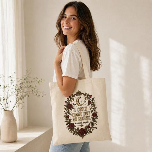 Smiling woman carrying the Natural "I Only Come Out at Night to Avoid People" gothic canvas tote bag by SarcasmArt over her shoulder – a gothic introvert gift.