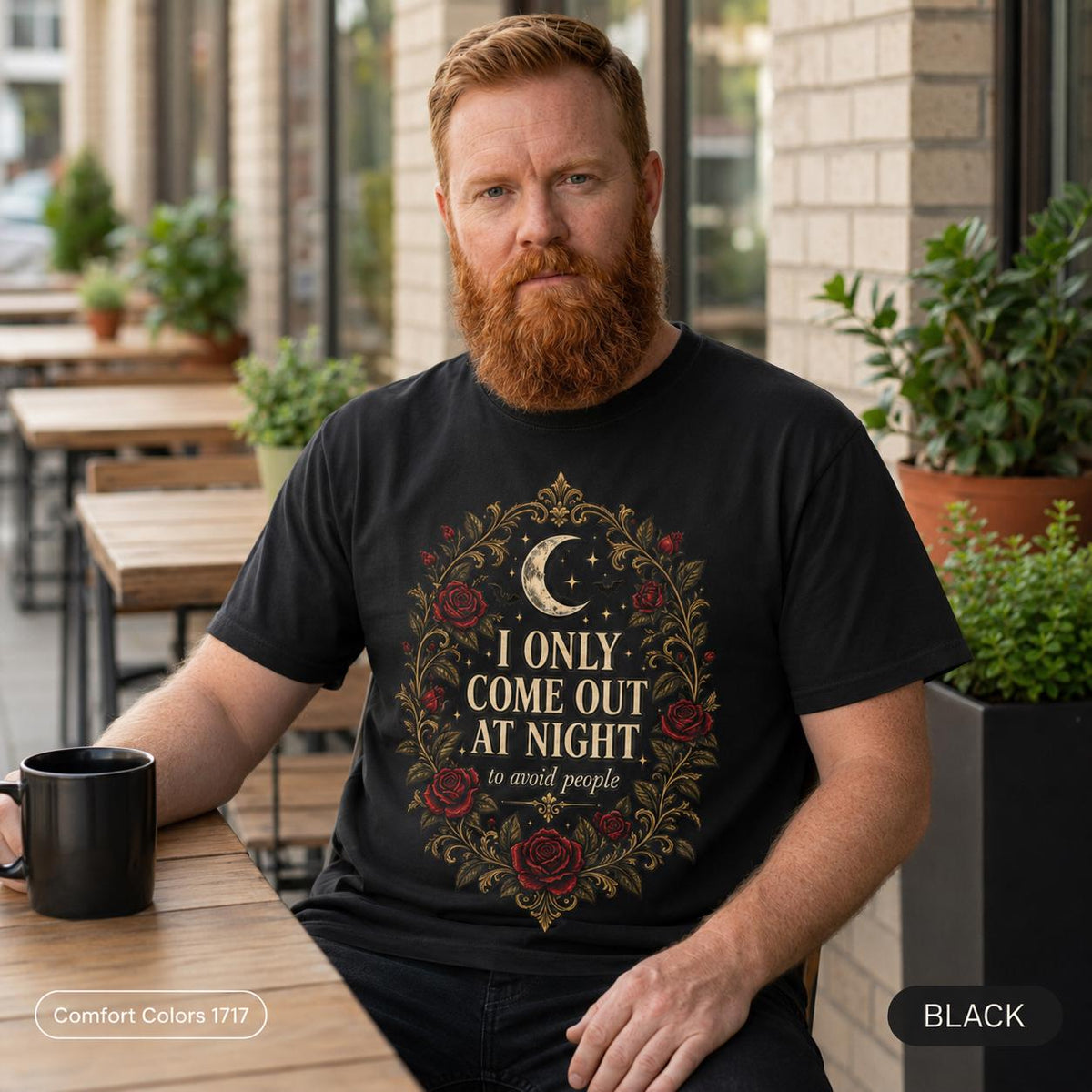 Bearded man with a coffee on a porch wearing the "I Only Come Out at Night" romantic gothic vampire T-shirt by SarcasmArt in Black – an anti-social humor tee with a crescent moon, bats and dark red Victorian roses in a gold filigree frame around the words I ONLY COME OUT AT NIGHT.
