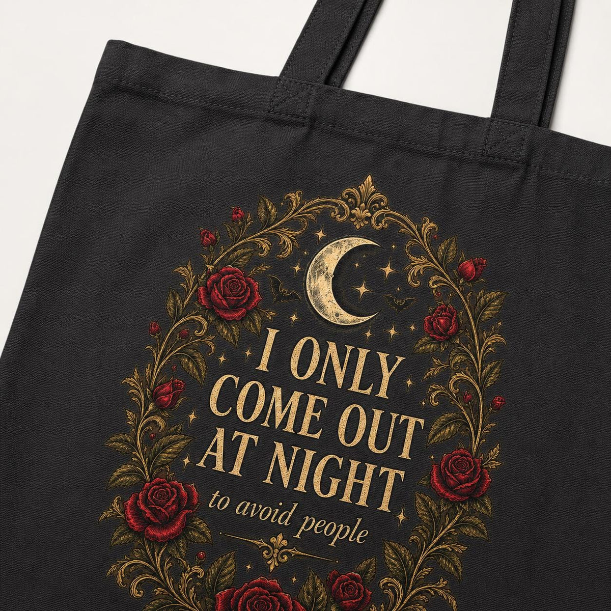 Print detail of the Black "I Only Come Out at Night to Avoid People" gothic canvas tote bag by SarcasmArt: a crescent moon and dark red Victorian roses in a gold filigree frame around the words I ONLY COME OUT AT NIGHT to avoid people.