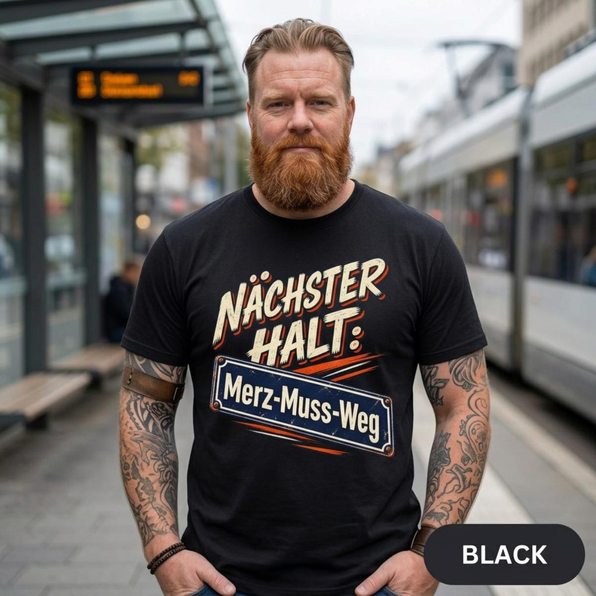 Bearded man on a train platform wearing the "Nächster Halt: Merz-Muss-Weg" German political satire T-shirt by SarcasmArt in Black.