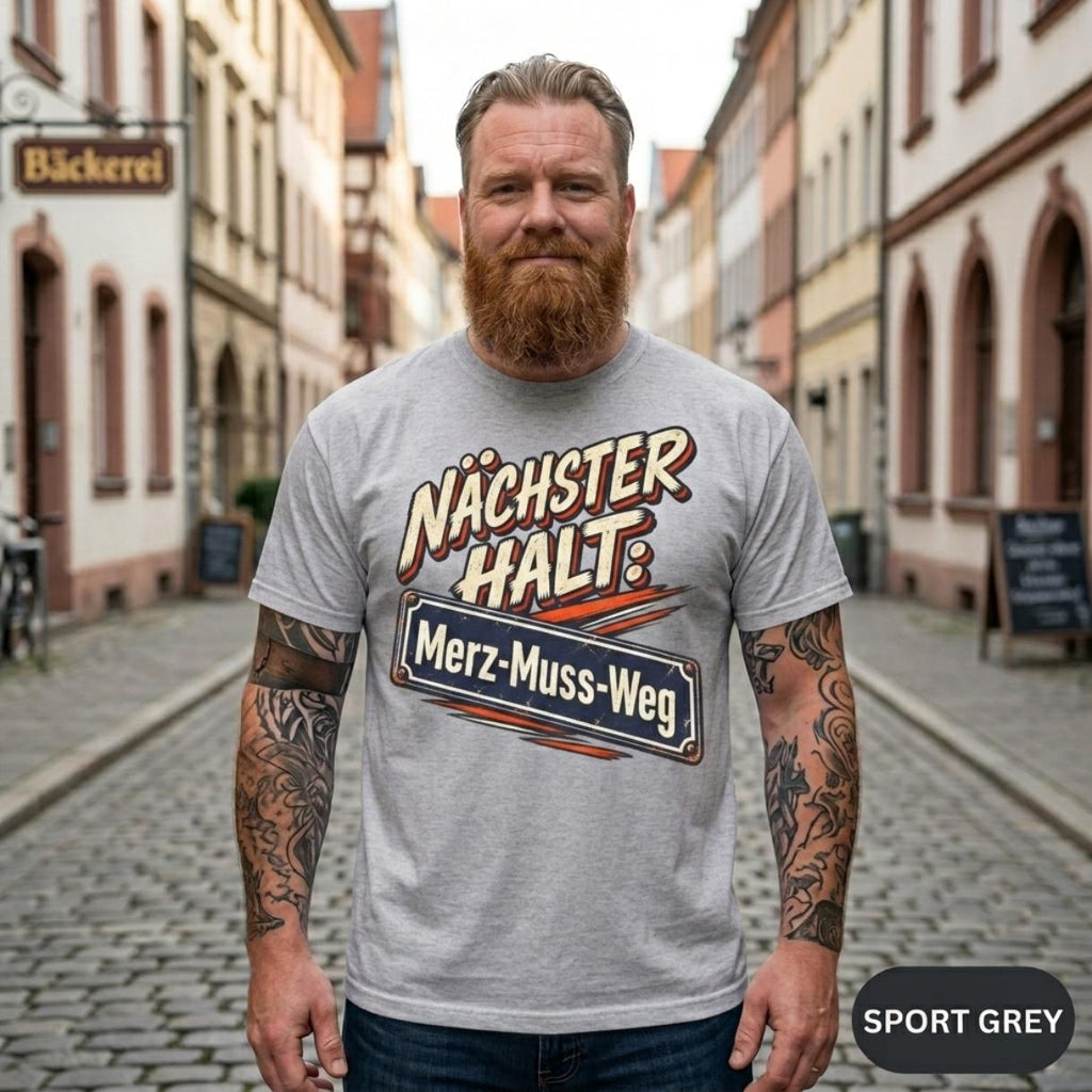 Bearded man on a German old-town street wearing the "Nächster Halt: Merz-Muss-Weg" German political satire T-shirt by SarcasmArt in Sport Grey.