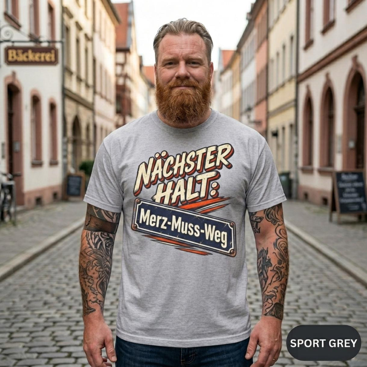 Bearded man on a German old-town street wearing the "Nächster Halt: Merz-Muss-Weg" German political satire T-shirt by SarcasmArt in Sport Grey.