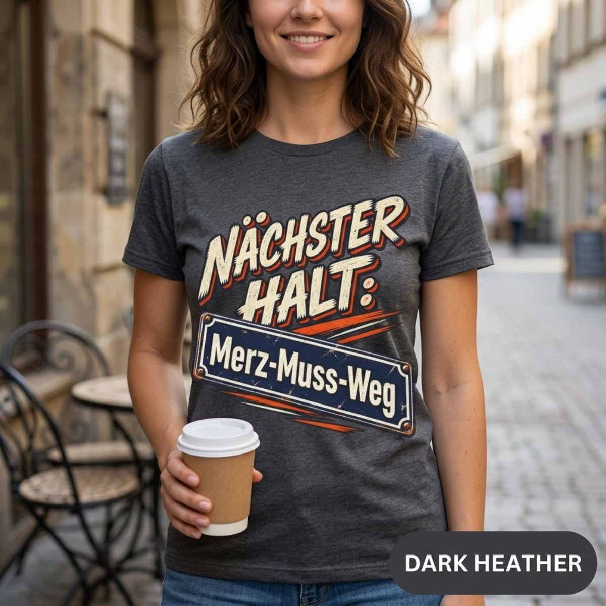 Woman with a coffee to go on a city street wearing the "Nächster Halt: Merz-Muss-Weg" German political satire T-shirt by SarcasmArt in Dark Heather.