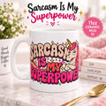 "Sarcasm Is My Superpower" unicorn coffee mug by SarcasmArt: white 11 oz glossy ceramic mug with an eye-rolling retro unicorn with a pink mane and bold pink and cream lettering SARCASM IS MY SUPERPOWER, on a pink desk.