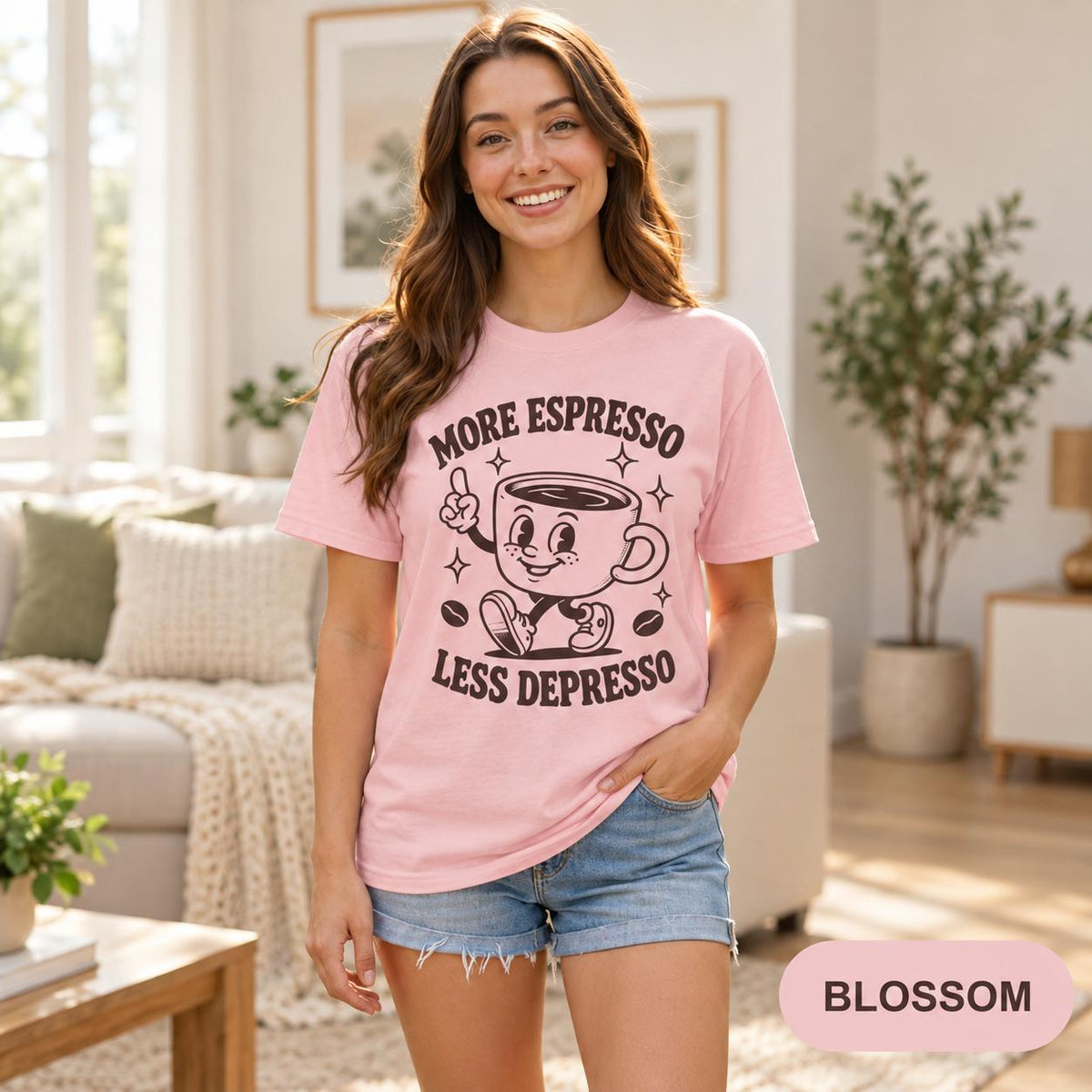 Woman in a bright living room wearing the "More Espresso, Less Depresso" retro coffee T-shirt by SarcasmArt in Blossom (soft pink).