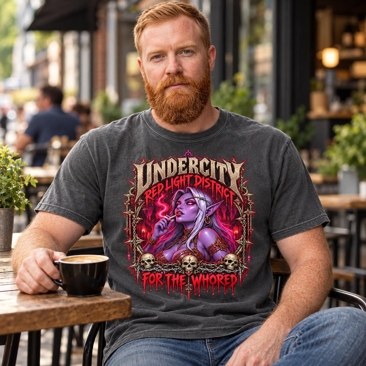 Bearded man at an outdoor café table wearing the "Undercity Red Light District" dark humor gamer T-shirt by SarcasmArt in Pepper (washed charcoal).
