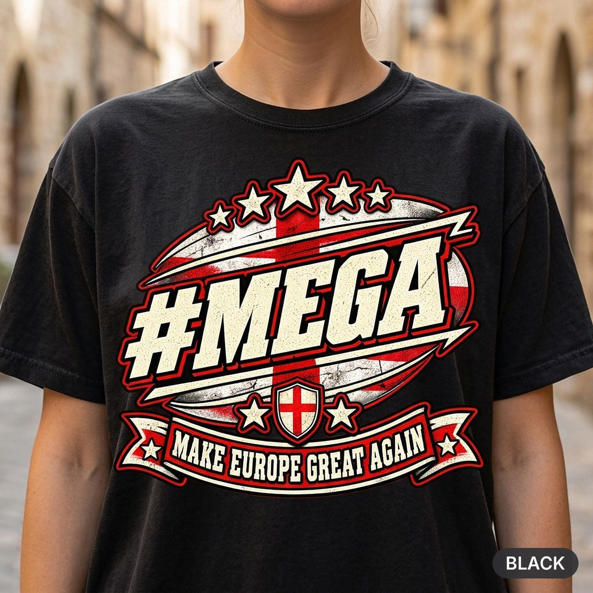 Close-up of the "#MEGA Make Europe Great Again" England T-shirt by SarcasmArt in Black: a retro #MEGA sports badge with the red St George cross on white, a St George cross shield, stars and a MAKE EUROPE GREAT AGAIN banner, printed large on a garment-dyed Comfort Colors 1717 tee.