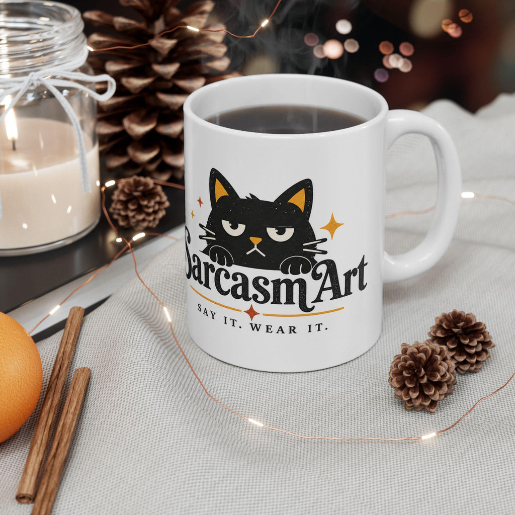 May include: A white ceramic mug featuring a graphic of a black cat with yellow inner ears and a grumpy expression. Below the cat, the text reads SarcasmArt in a bold black font, followed by the smaller text SAY IT. WEAR IT. with orange star accents.