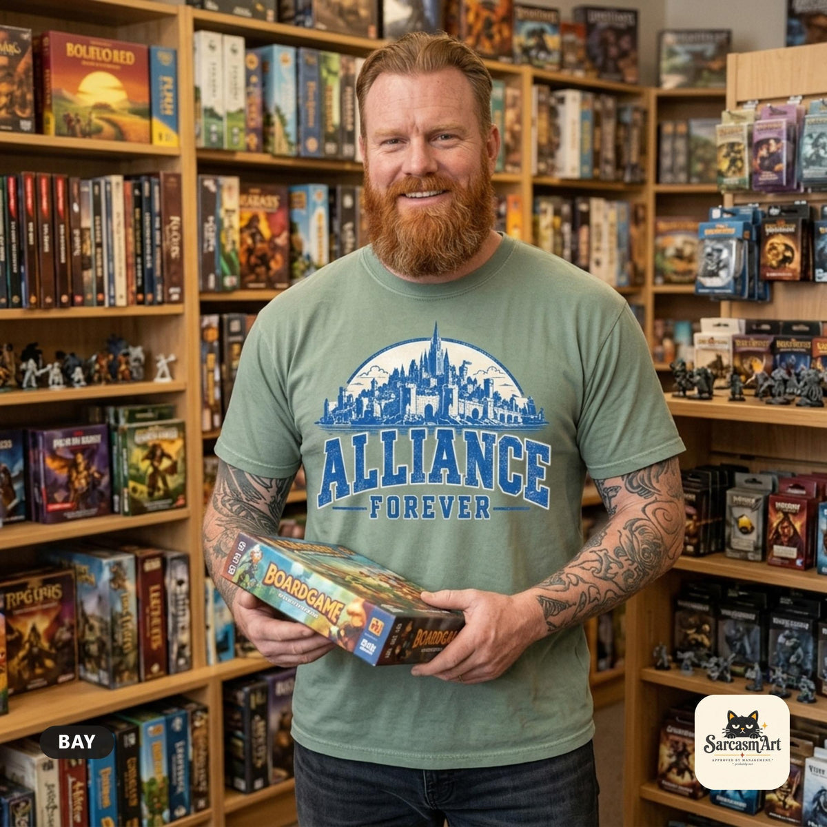 Bearded man holding a board game in a game store wearing the "Alliance Forever" World of Warcraft gamer T-shirt in Bay (sage green) – a Comfort Colors 1717 unisex tee by SarcasmArt with blue distressed ALLIANCE FOREVER varsity lettering under a fantasy city skyline.