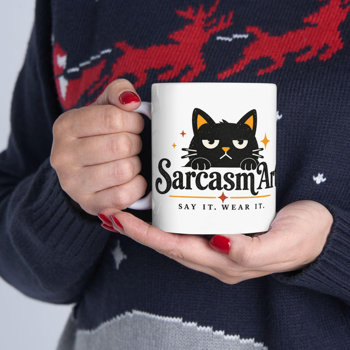 May include: A white ceramic mug featuring a graphic of a black cat with yellow inner ears and a grumpy expression. Below the cat, the text reads SarcasmArt in a stylized black font, followed by the smaller text SAY IT. WEAR IT. in black.