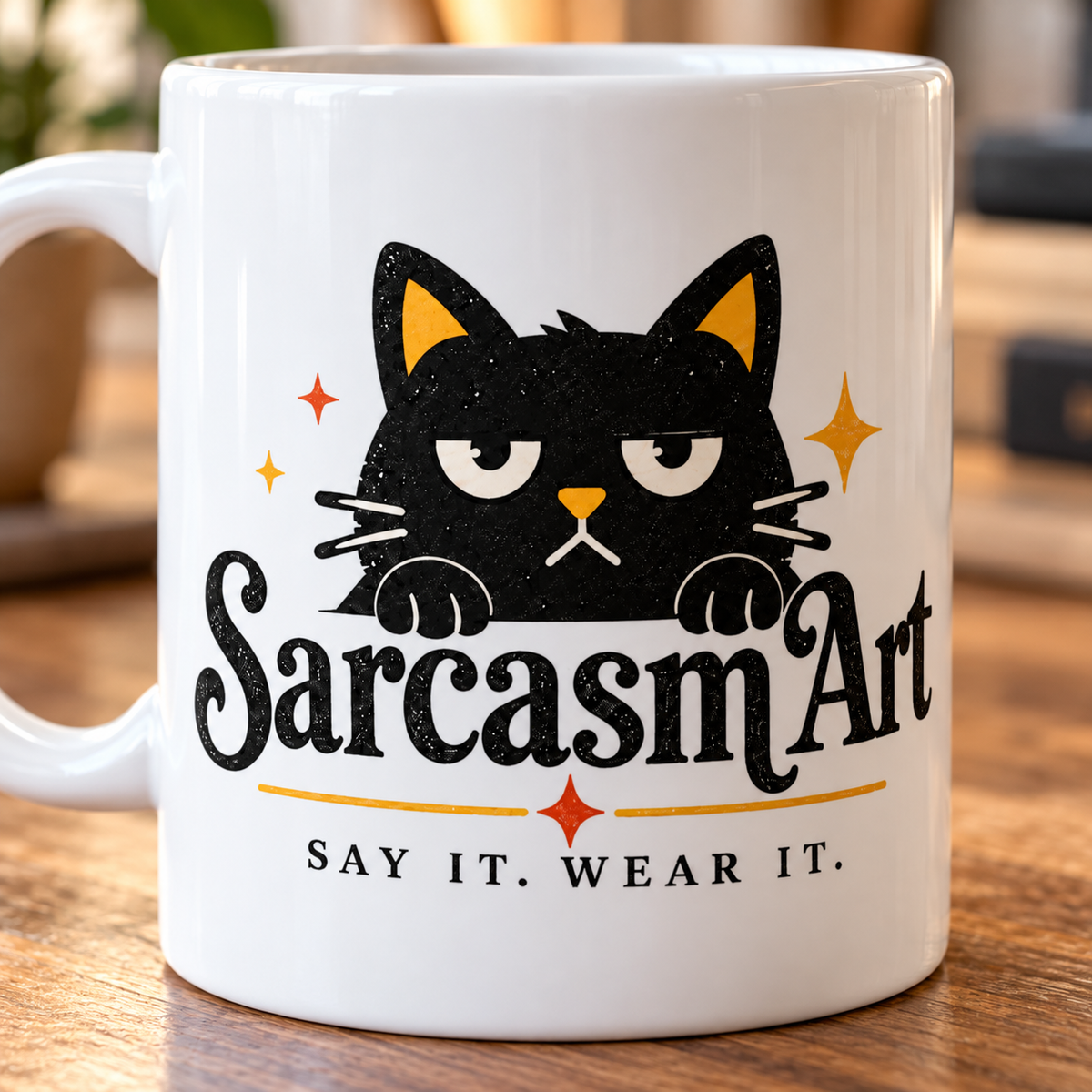 Print close-up of the sarcastic cat coffee mug by SarcasmArt: grumpy black cat peeking over the SarcasmArt script logo with sparkles and the tagline SAY IT. WEAR IT. on white glossy ceramic.